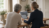 Uitvaartondernemer vult samen met een nabestaande aan tafel een online rouwkaart in op een tablet